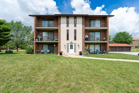 Front view of a three-story brick apartment building with balconies.