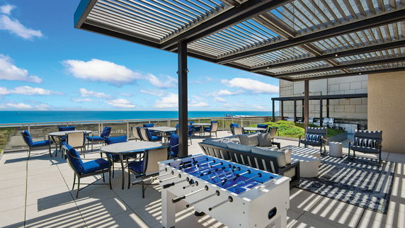 Rooftop patio with seating area, tables, and a foosball table, featuring a view of the ocean.