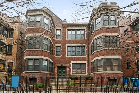 Front view of a multi-story brick apartment building with bay windows.