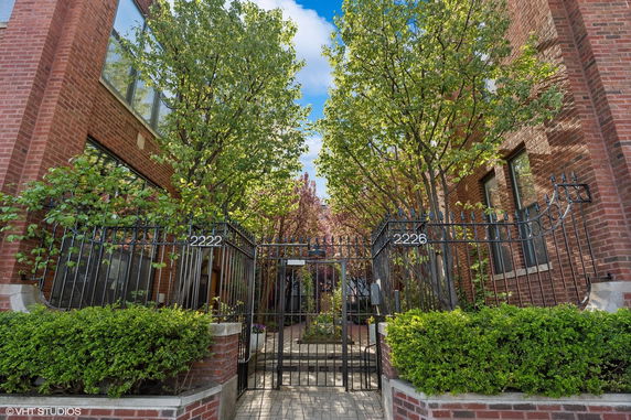 Front view of a brick residential building with iron gate and trees.