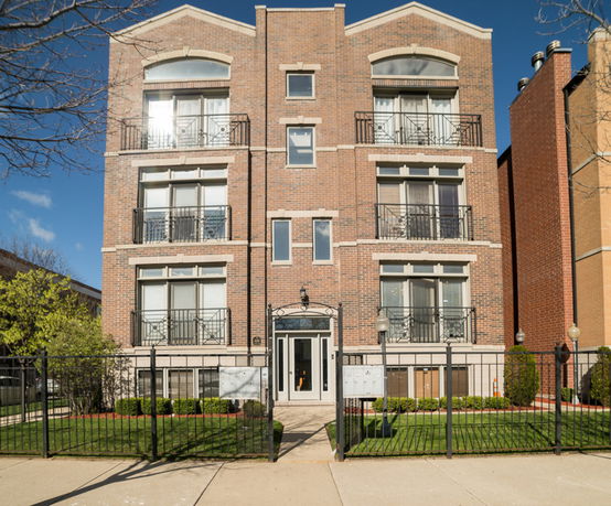 Front view of a multi-story brick building with balconies and a fenced entrance.