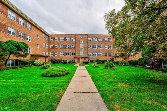 Front view of a multi-story apartment building with a central walkway and greenery.