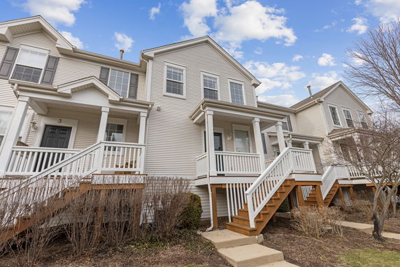 Front view of a two-story townhouse with white siding and wooden steps leading to the entrance.