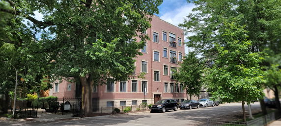 Front view of a multi-story brick building with several windows, surrounded by trees.