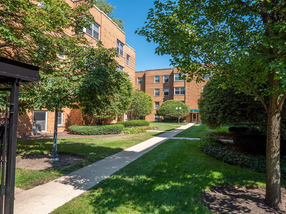 Front view of a multi-story brick apartment building with a pathway leading to the entrance.