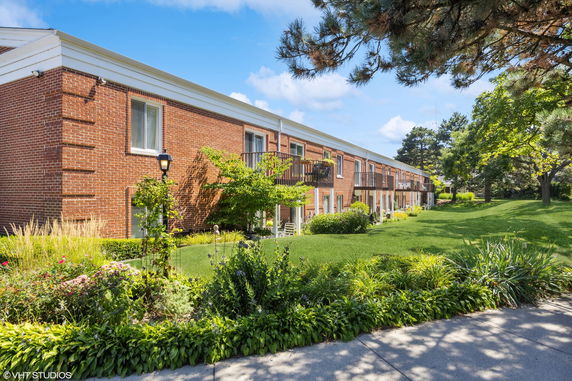 Front view of a two-story brick building with balconies and a well-maintained garden.