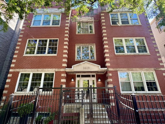 Front view of a multi-story brick apartment building with large windows and a gated entrance.