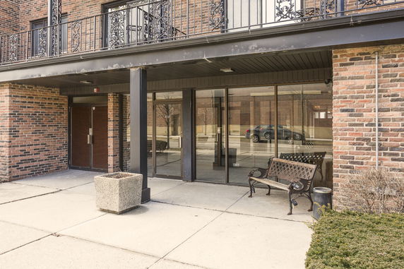Front view of a brick building with a glass entrance and a small bench.