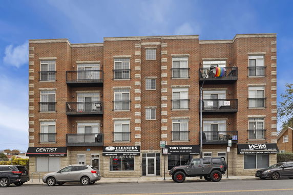 Front view of a multi-story brick building with balconies and ground-floor shops.