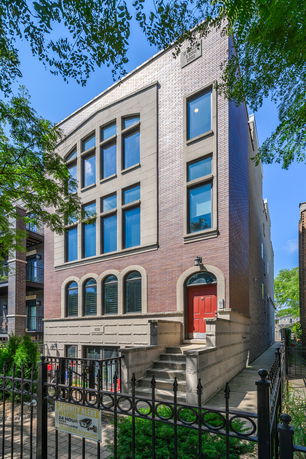 Front view of a multi-story brick building with large windows and a red door.