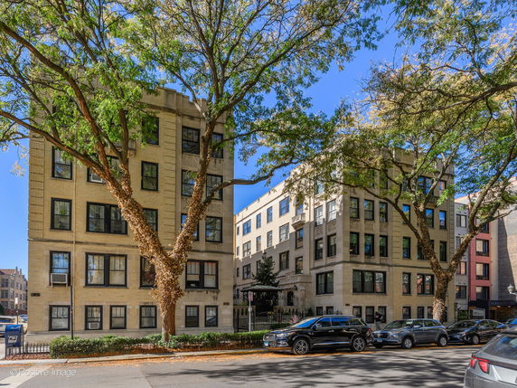 Front view of a multi-story residential building with multiple windows and trees in front.