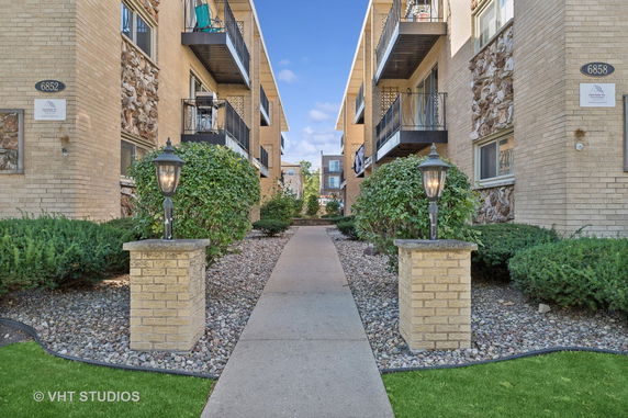 Front view of an apartment building with balconies and a pathway leading to the entrance.