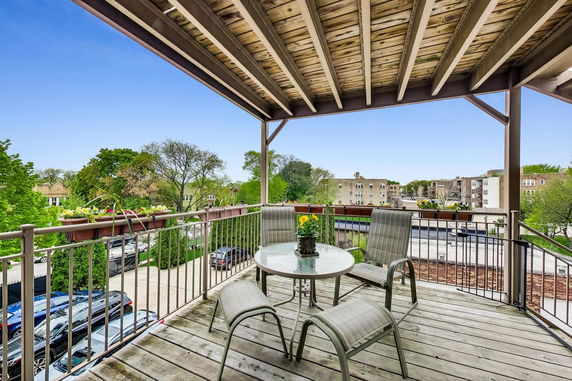 Outdoor balcony with a table and chairs overlooking surrounding residential area.