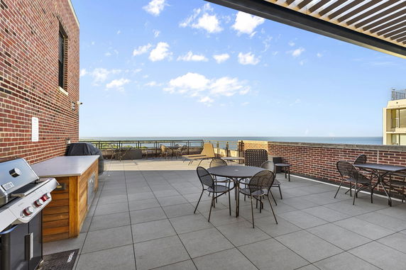 Rooftop with seating and grilling area, featuring a brick wall and ocean view.