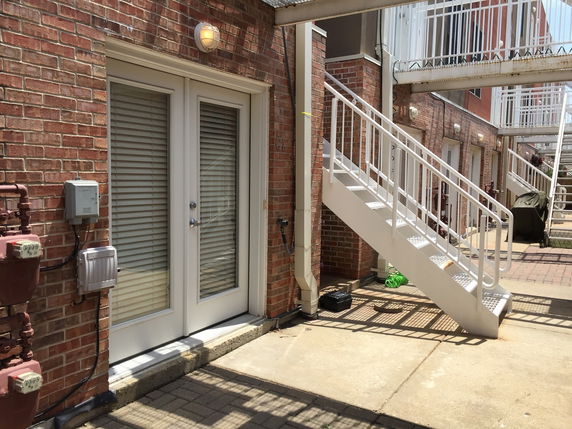 Exterior view of a building with brick walls, glass-paneled doors, and white metal stairs.