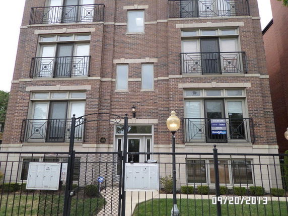 Front view of a multi-story brick apartment building with balconies and gated entrance.