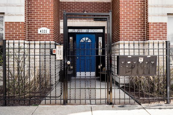 Front view of the entrance to a brick building with a blue door and metal gate.