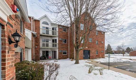 Front view of a multi-story brick apartment building with balconies and a snowy landscape.