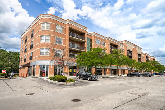 Front view of a multi-story brick building with storefronts and a parking area.