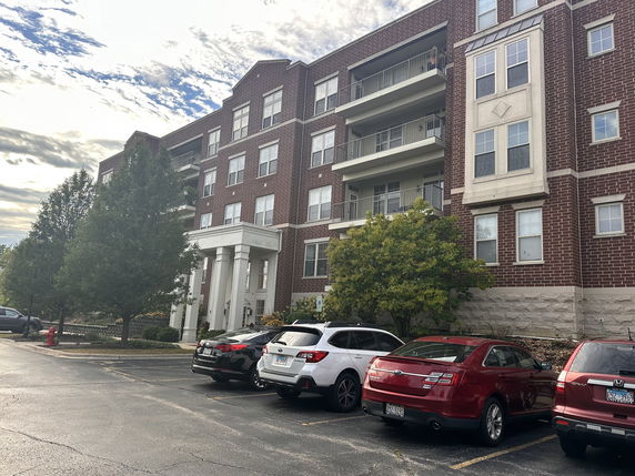 Front view of a multi-story brick building with balconies and a parking area.