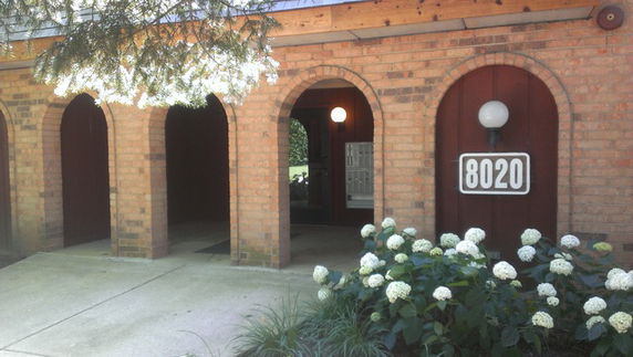 Front view of a brick house with arched entrances and a lamp above the number 8020.