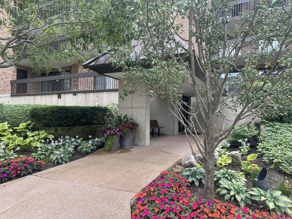 Front view of a mid-rise apartment building with balconies and a landscaped entrance.