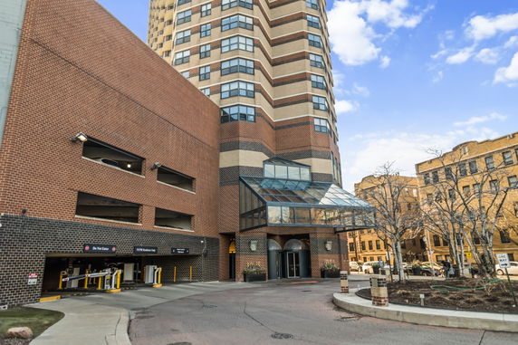 Front view of a high-rise building with a glass entrance canopy and parking area.