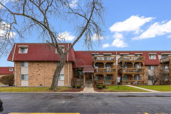 Front view of a multi-story brick apartment building with wooden balconies and a red roof.