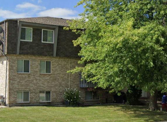 Front view of a multi-story brick building with a shingled mansard roof.
