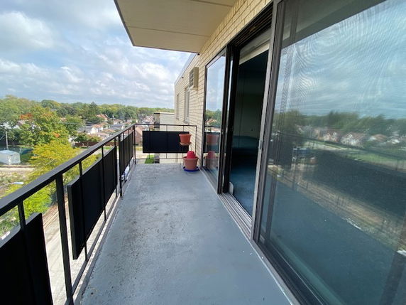 A balcony view from a building overlooking a residential area with trees and houses in the background.