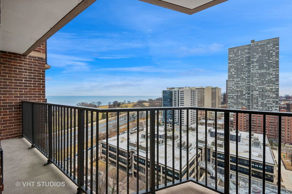 View from a balcony overlooking a cityscape with high-rise buildings and a body of water in the distance.