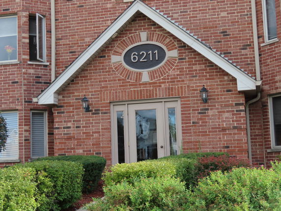 Front view of a brick house with an entrance door and number 6211 above it.