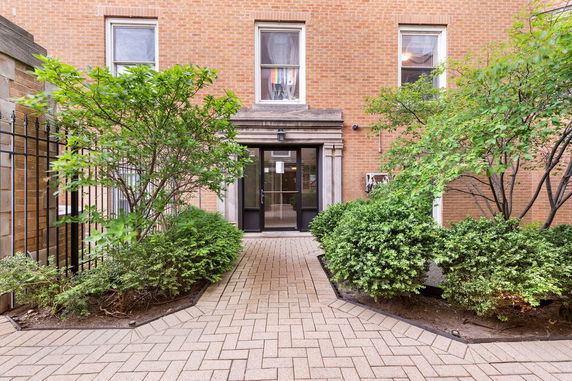 Front view of a brick building entrance with shrubs and a pathway.