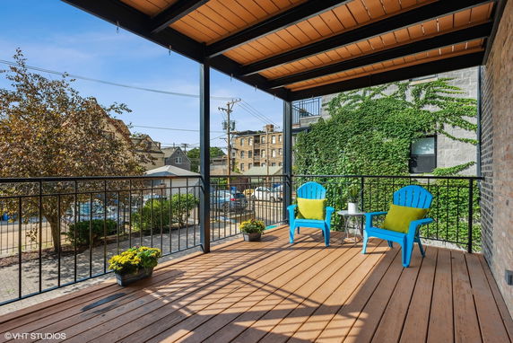 Rooftop deck with blue chairs and small tables, overlooking neighboring buildings and greenery.