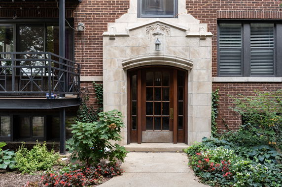 Front view of a brick building entrance with an arched doorway and decorative stonework.