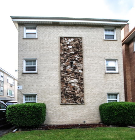 Front view of a three-story brick building with rectangular windows and a decorative stone panel in the center.