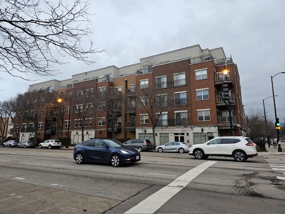 Front view of a multi-story apartment building with brick exterior and street parking.