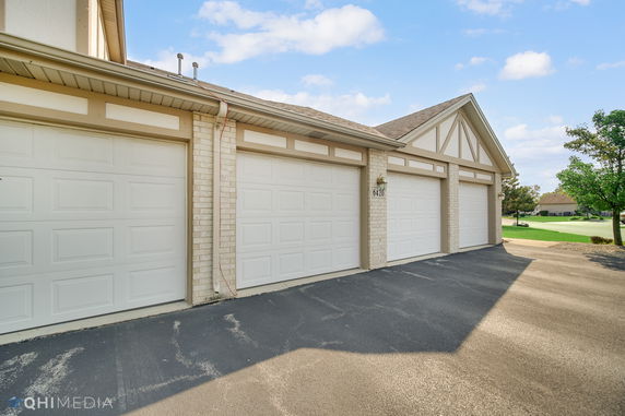 Front view of a row of garages attached to a building with white brick and beige accents.