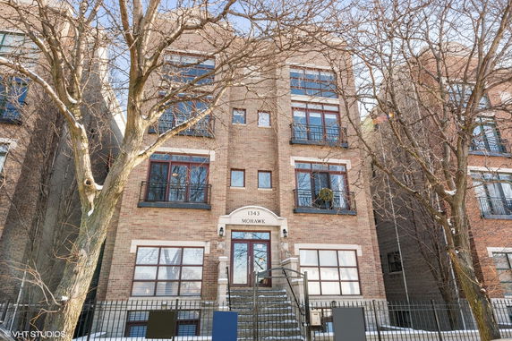Front view of a multi-story brick building with balconies and a central entrance stairway.