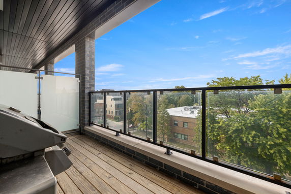 Outdoor terrace with railing and view of surrounding buildings and trees.