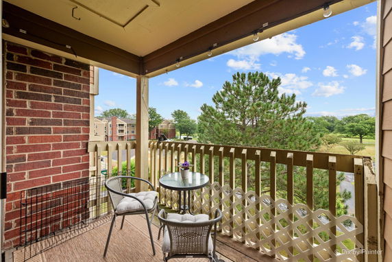 Balcony view showing a seated area with chairs and a table, overlooking a tree and distant buildings.