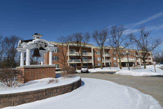 Front view of a brick apartment building with balconies and a small structure with a bell in the foreground.