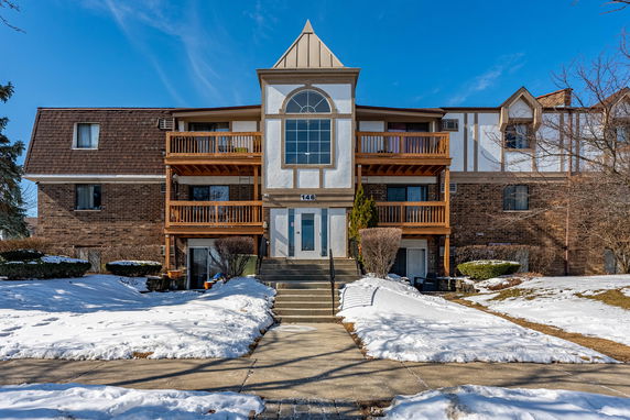 Front view of a multi-story building with wood balconies and a central entrance, surrounded by snow-covered ground.