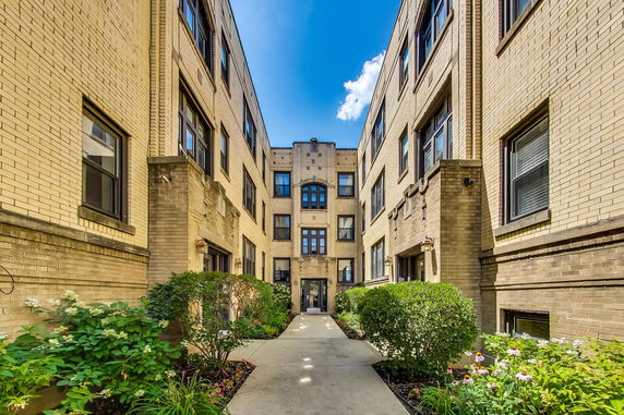 Front view of a multi-story brick apartment building with a central courtyard entrance.