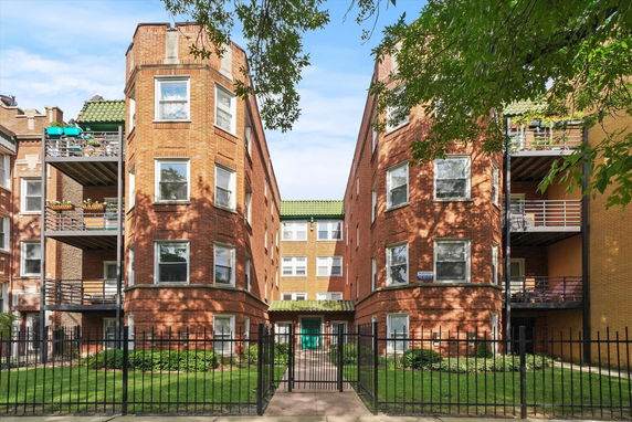 Front view of a multi-story brick building with balconies and a gated entrance.