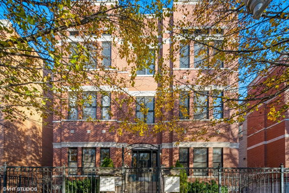 Front view of a multi-story brick building with large windows and a gated entrance.