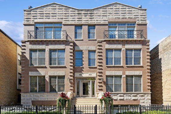 Front view of a brick three-story residential building with large windows and dual entryways.