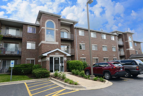 Front view of a brick three-story apartment building with balconies and an entrance canopy.
