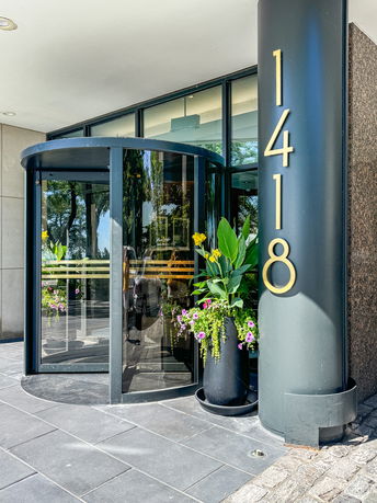 Entrance of a building with large glass windows and a revolving door. The building's address '1418' is prominently displayed on a column beside the door.