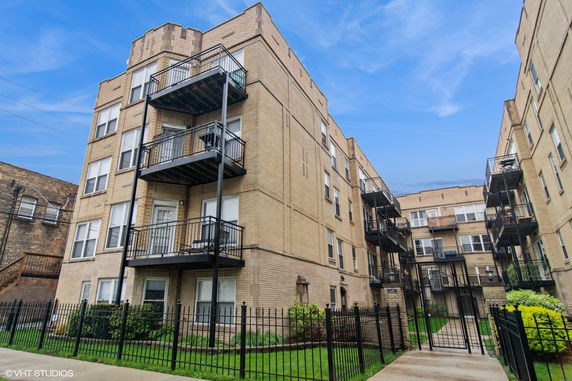 Front view of a multi-story apartment building with balconies and wrought iron fencing.